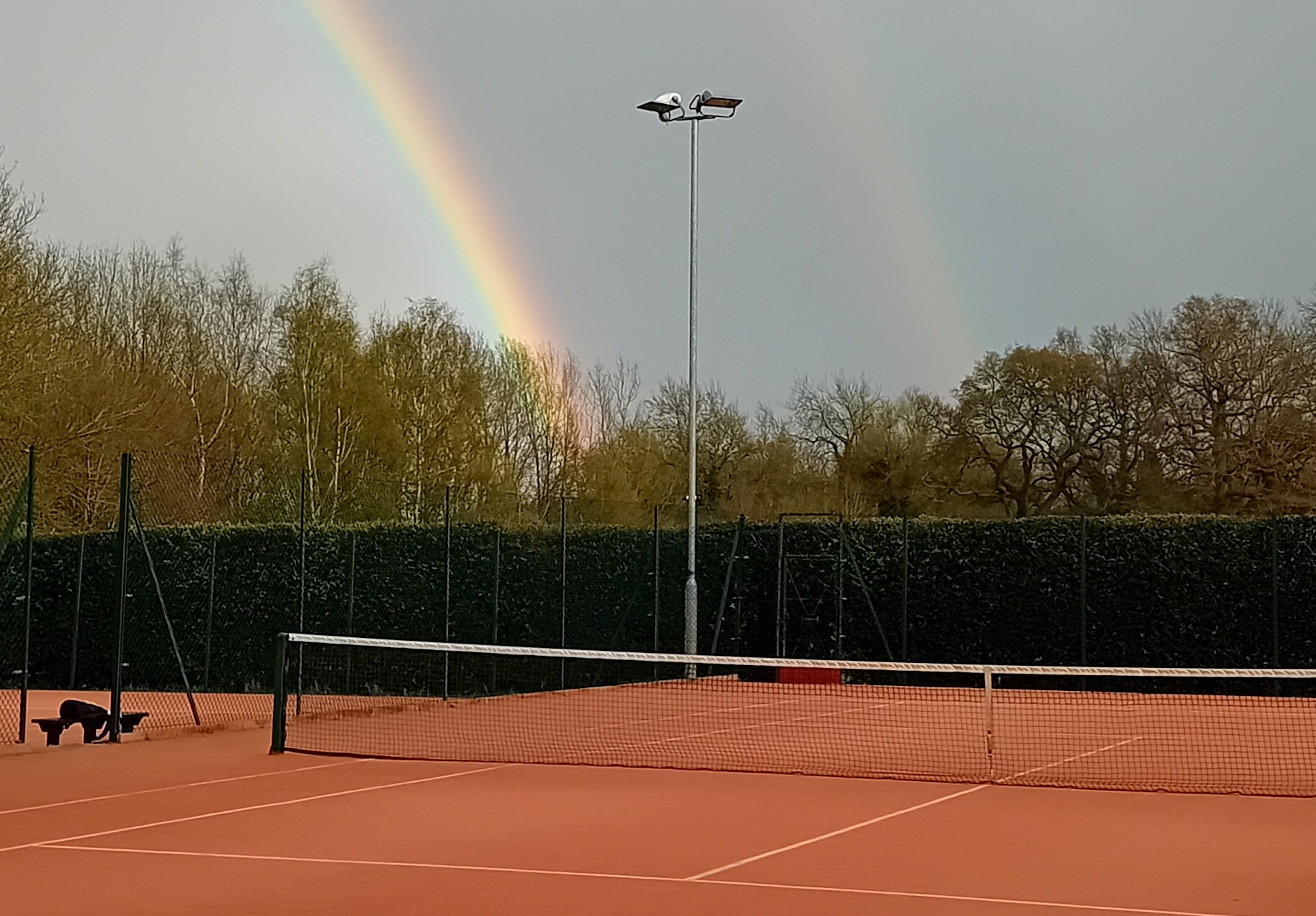 A picture of clay tennis courts, with a rainbow visible in the background