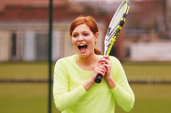 Woman laughing and holding tennis racket over her shoulder 