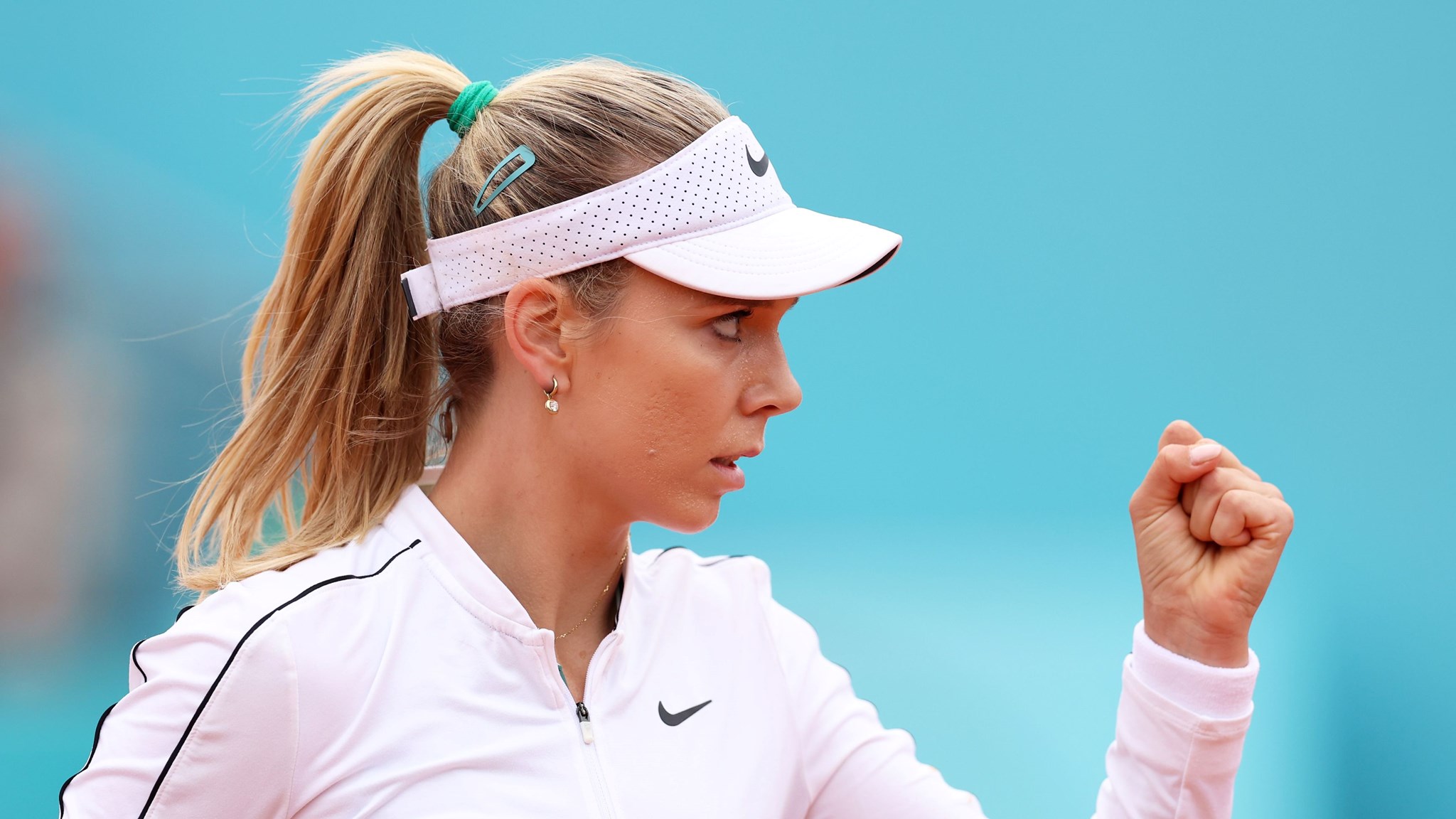 Katie Boulter, wearing a white Nike fleece and hat, clenching her fist in celebration on court at the Madrid Open