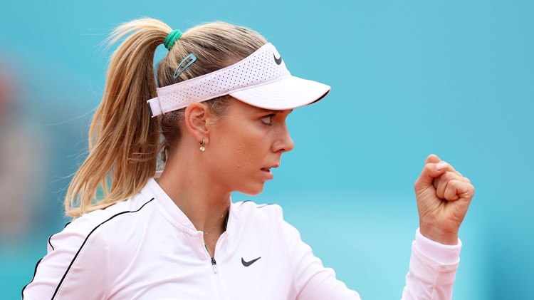 Katie Boulter, wearing a white Nike fleece and hat, clenching her fist in celebration on court at the Madrid Open
