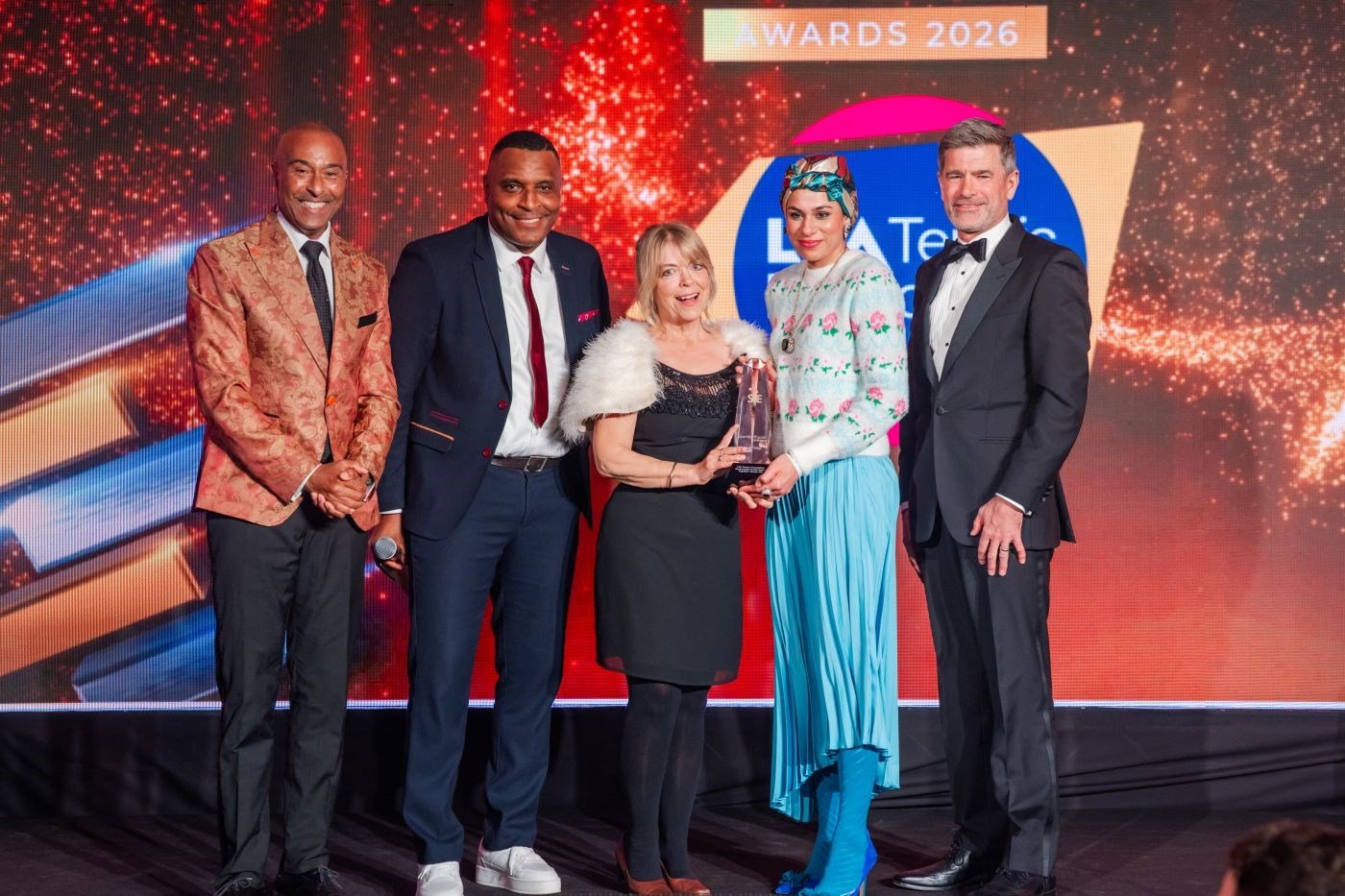 Fi8ve people on stage at sporting equals awards. Two females wining the award with presenters. 