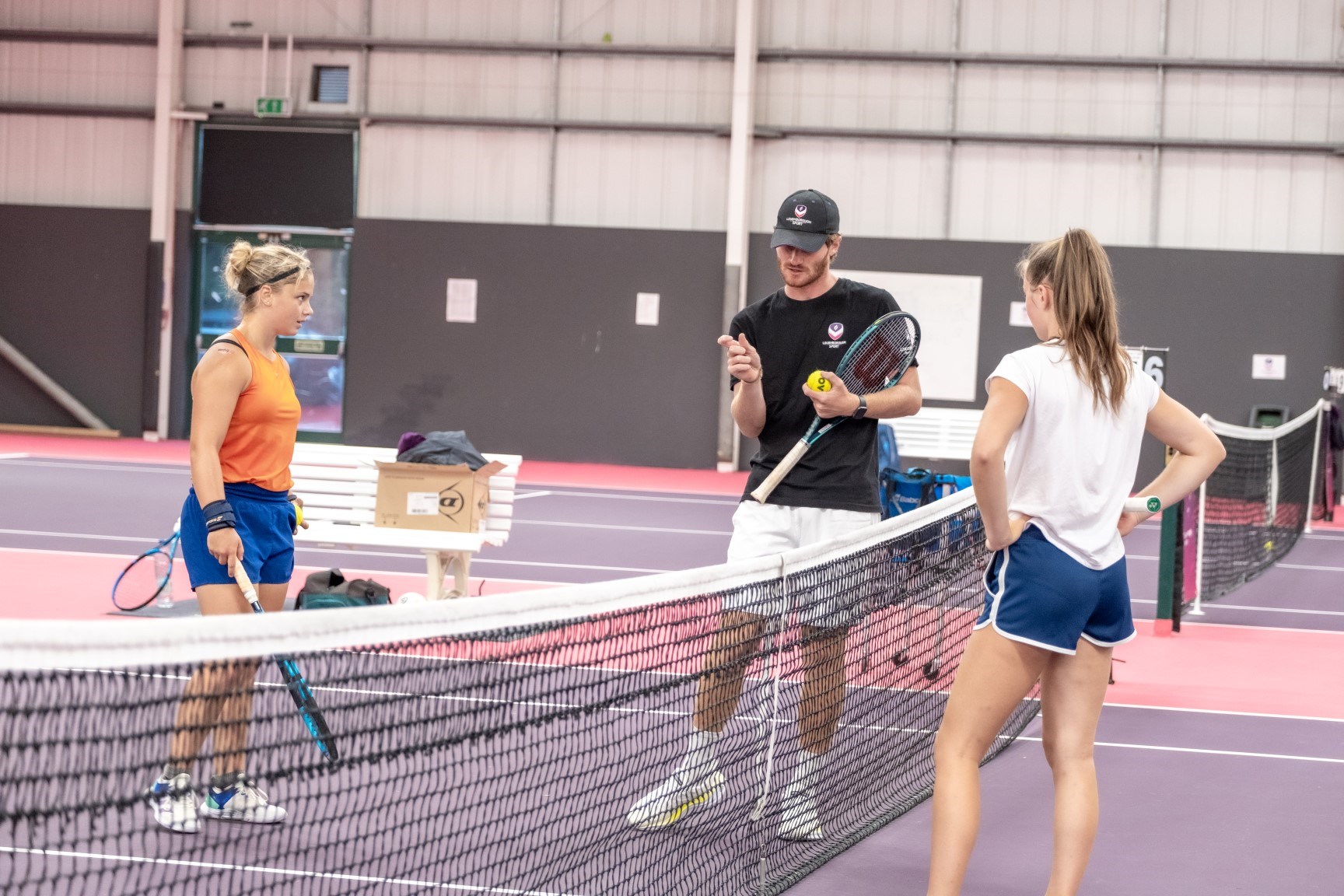 Two players on opposite sides of the net with a coach in the middle giving analysis