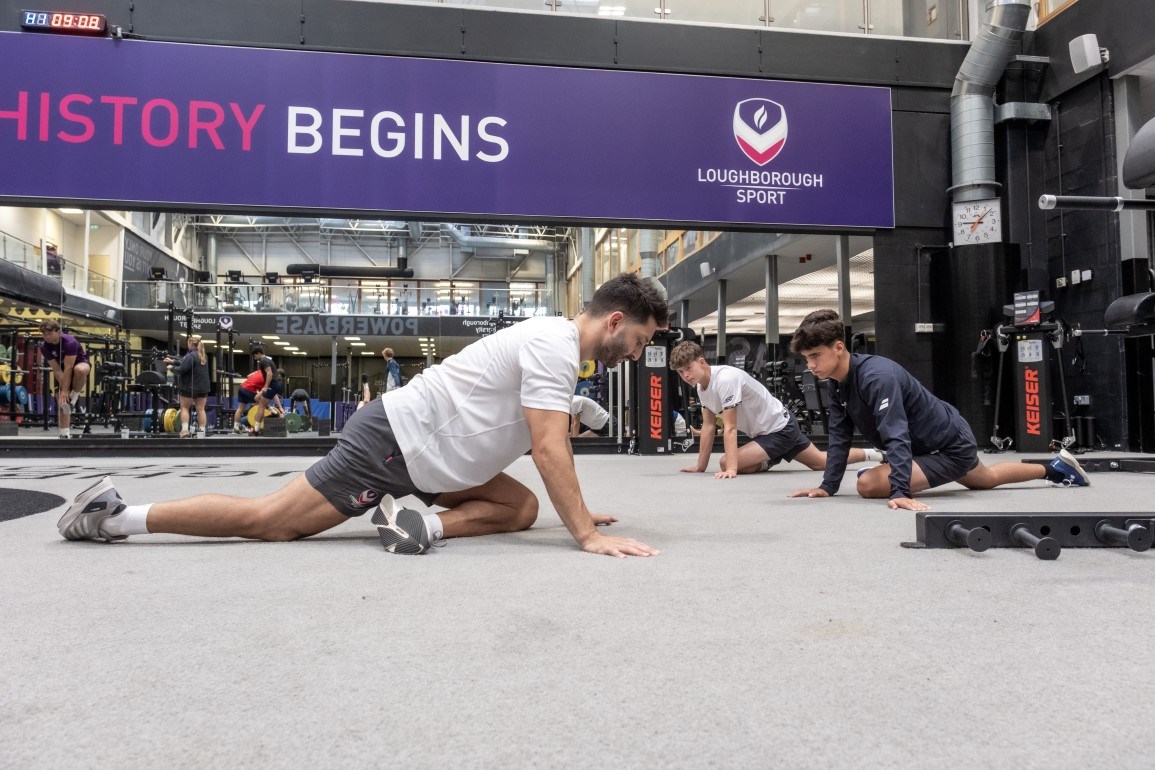 Three students stretching on the floor of the gym