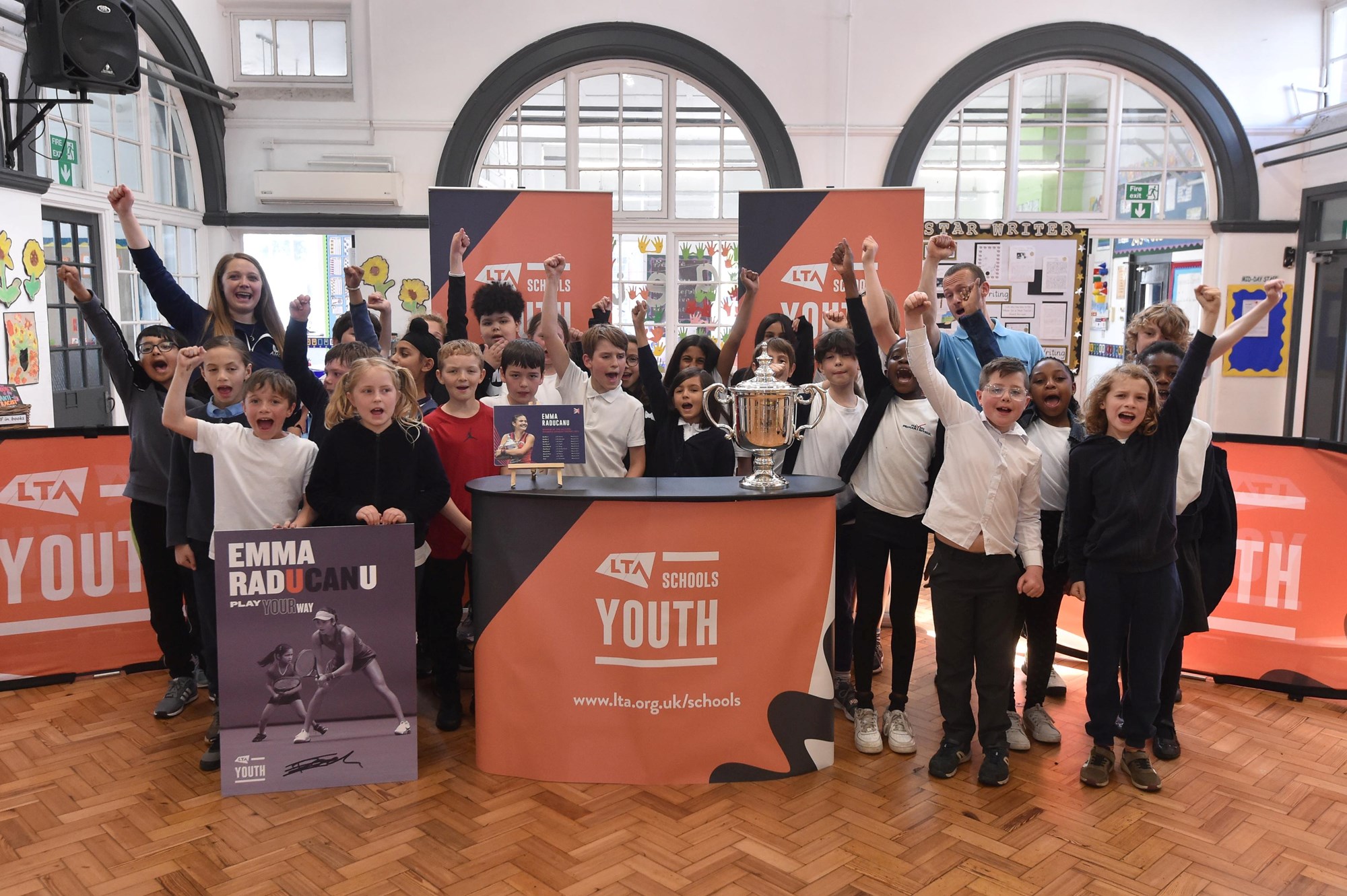 Pupils and teachers of Haydn Primary School in Nottinghamshire posing and cheering next to Emma Raducanu's US Open Trophy