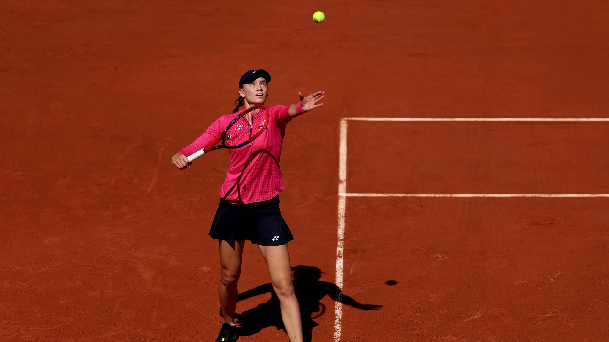 Elena Rybakina stood on a clay court while throwing a tennis ball in the air as she prepares to serve