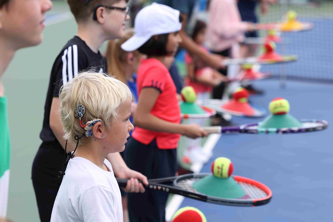 A group of children wearing hearing aids and holding tennis rackets and balls