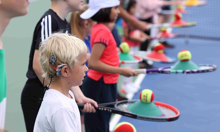 A group of children wearing hearing aids and holding tennis rackets and balls