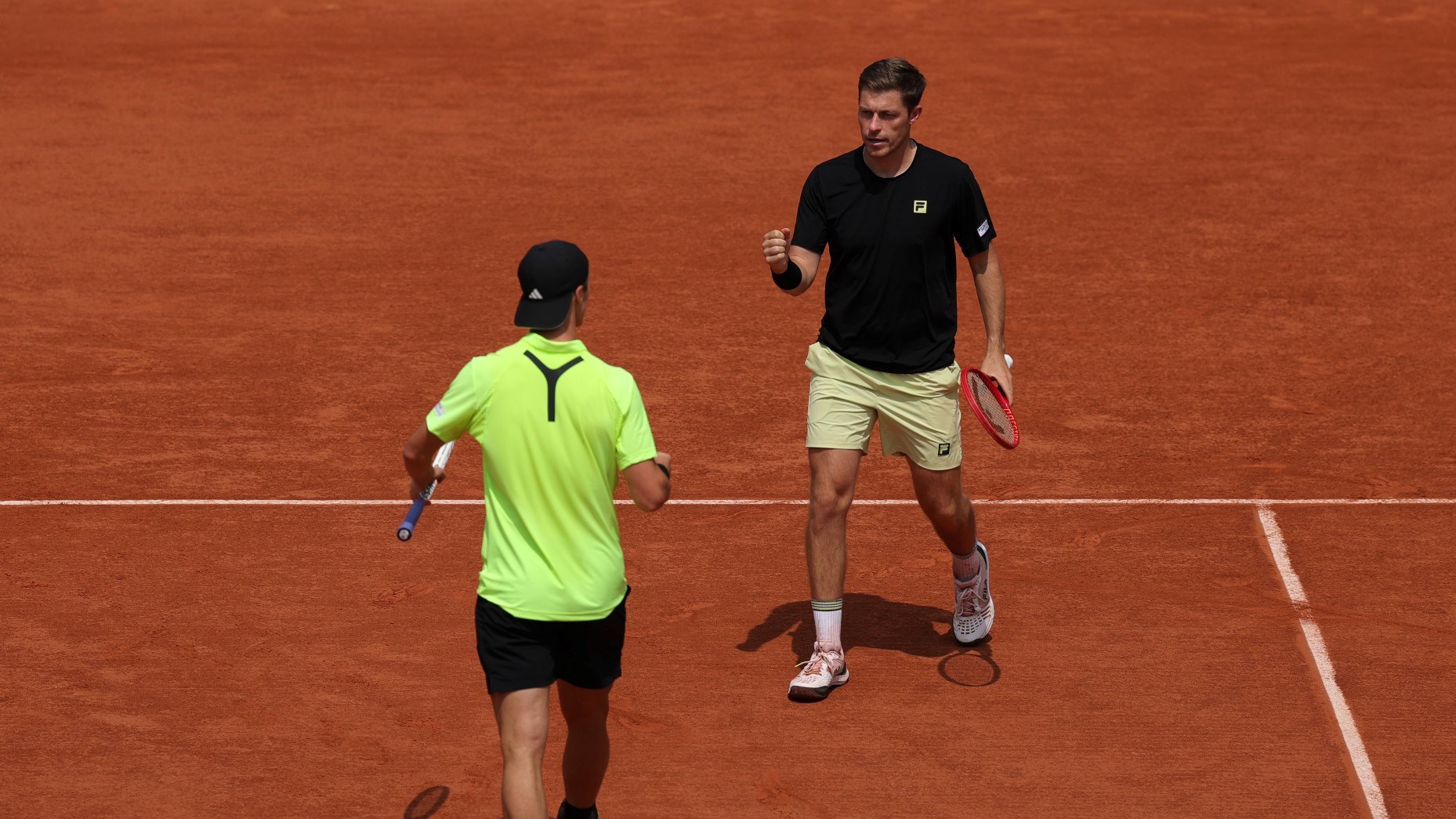 Neal Skupski walking with his fist pumped in celebration towards his partner Joe Salisbury who's doing the same celebration on the Roland Garros clay court