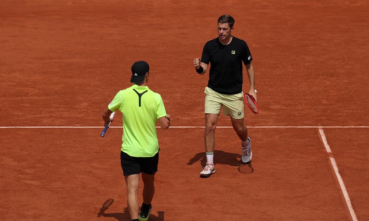 Neal Skupski walking with his fist pumped in celebration towards his partner Joe Salisbury who's doing the same celebration on the Roland Garros clay court