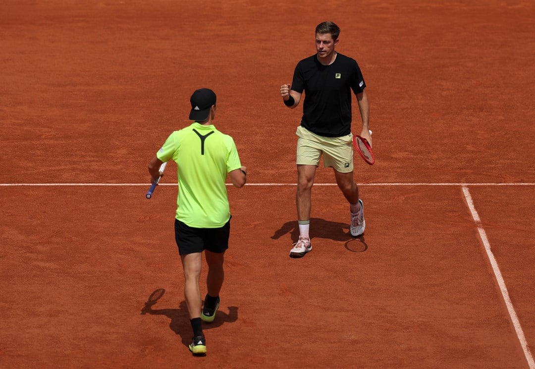 Neal Skupski walking with his fist pumped in celebration towards his partner Joe Salisbury who's doing the same celebration on the Roland Garros clay court