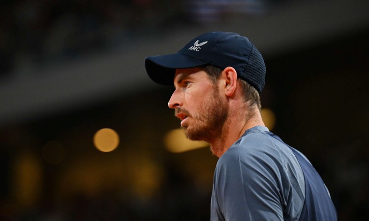 Andy Murray stood staring ahead on court while wearing a baseball cap