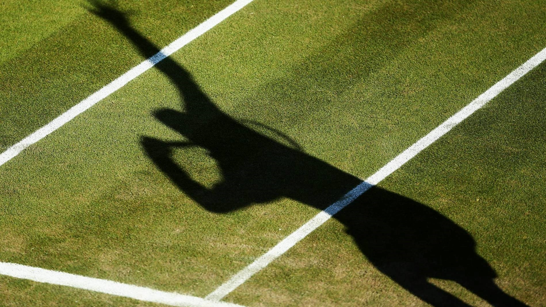 Shadow of a tennis player serving on the grass