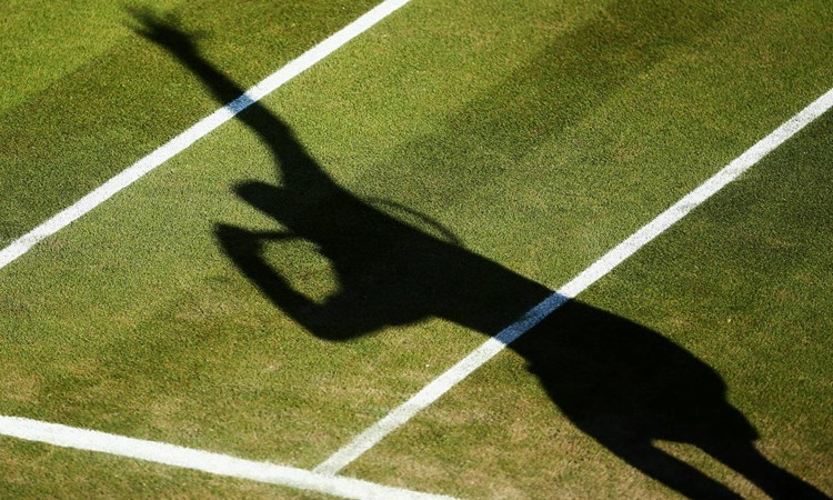 Shadow of a tennis player serving on the grass