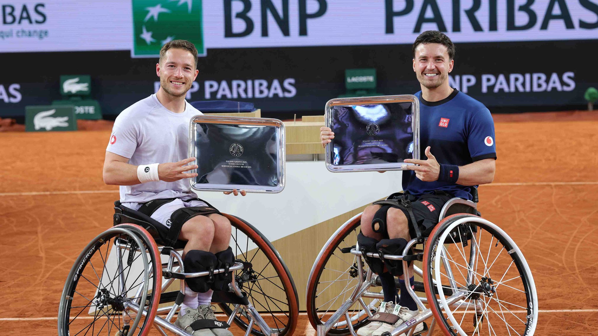 Alfie Hewett and Gordon Reid smiling while holding their winners trophies at Roland Garros