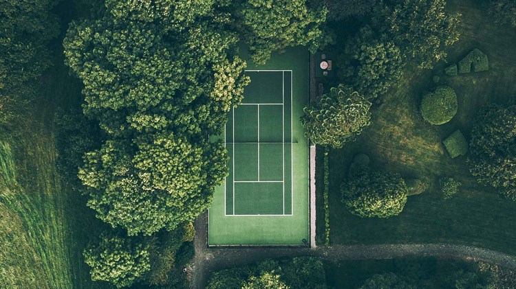 A green tennis court surrounded by green trees and grass