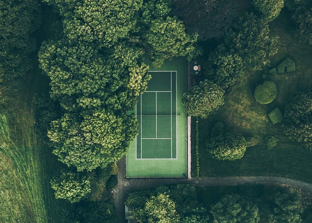 A green tennis court surrounded by green trees and grass