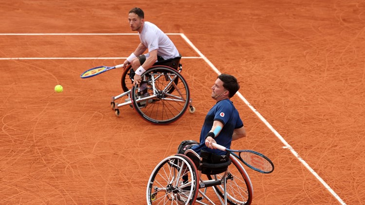 Gordon Reid about to hit a forehand on the clay with his partner Alfie Hewett looking on