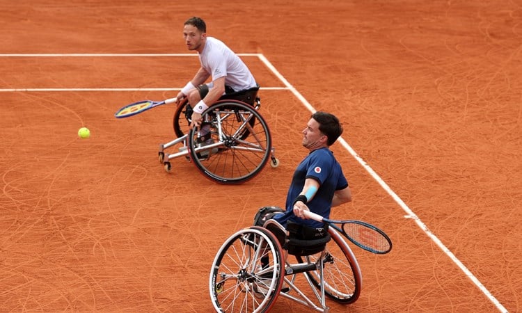 Gordon Reid about to hit a forehand on the clay with his partner Alfie Hewett looking on