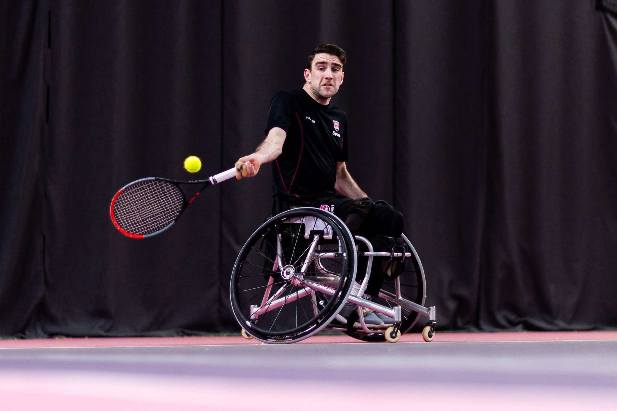 A man in a wheelchair hits a tennis ball