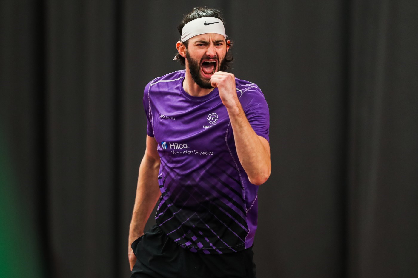 A man dressed in a purple shirt wearing a white headband clenches his fist in celebrating