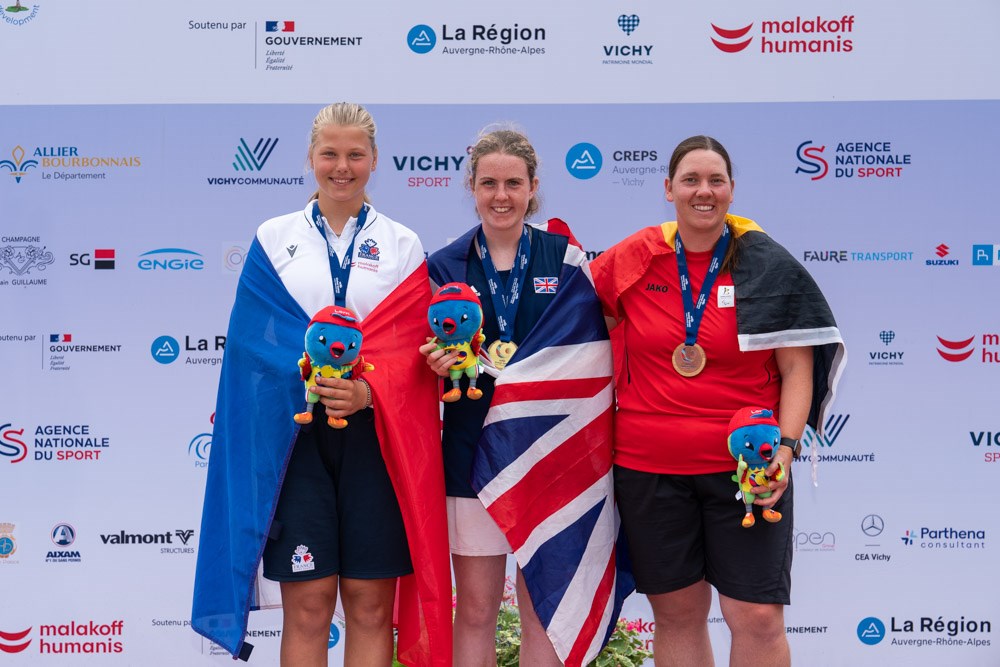 Gold medallist Anna McBride pictured on the winners' podium alongside her fellow competitors, holding the Virtus Global Games mascot.