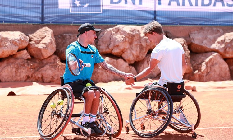 Andy Lapthorne and Niels Vink sat in their wheelchairs holding tennis rackets and shaking hands on court