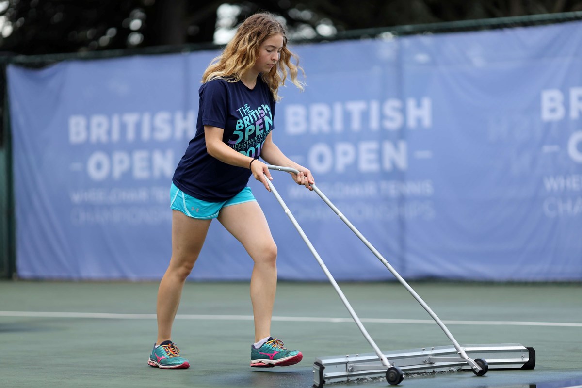 A female tennis volunteer clearing water from a tennis court after the rain