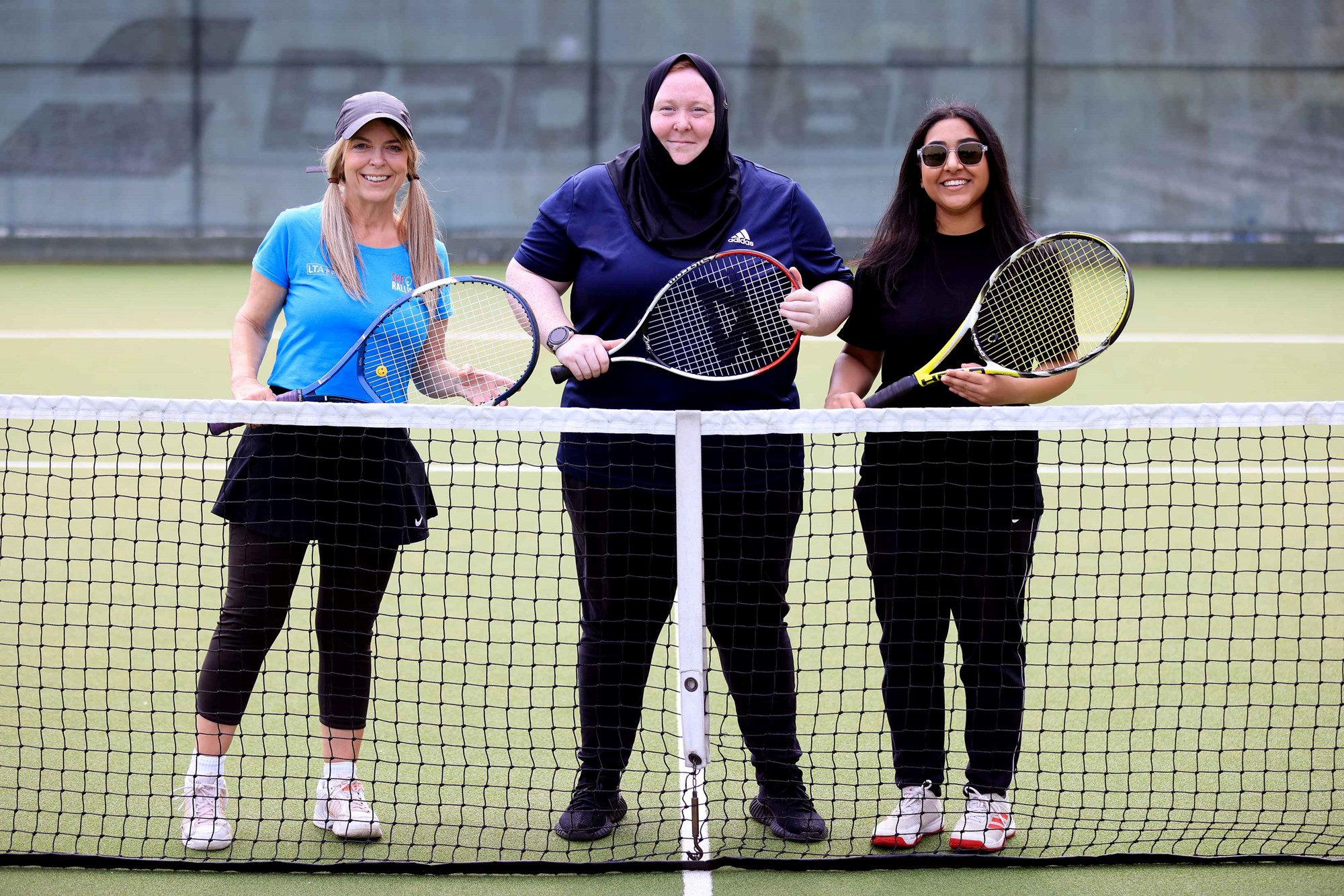 Carolle Forde Garcia (L), Nalette Tucker, and Iman Mahmood (R) pictured stood behind the net with tennis rackets in hand.