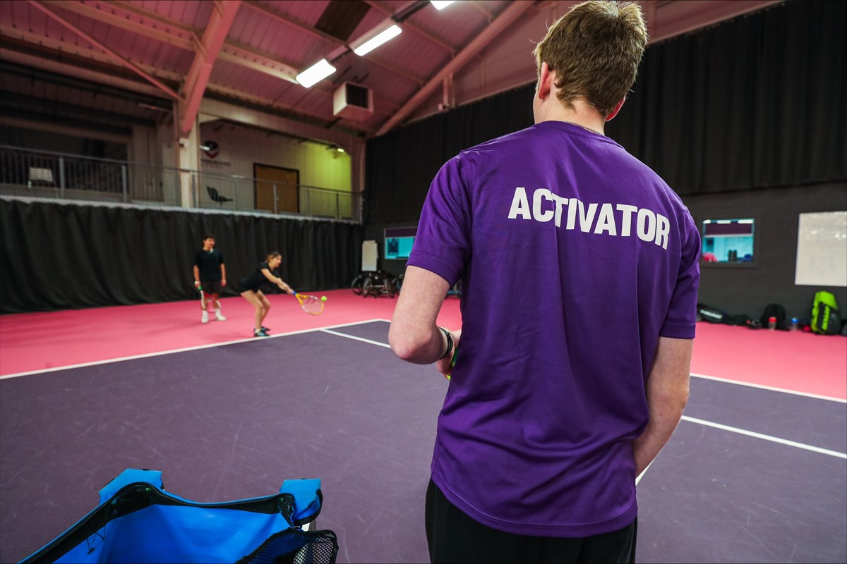 A University Activator coaching university tennis players on an indoor court