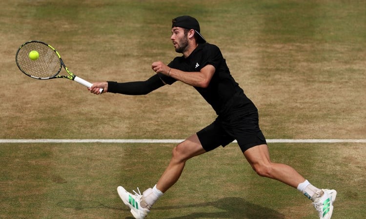 Jacob Fearnley reaches to hit a ball with his racket on a grass court