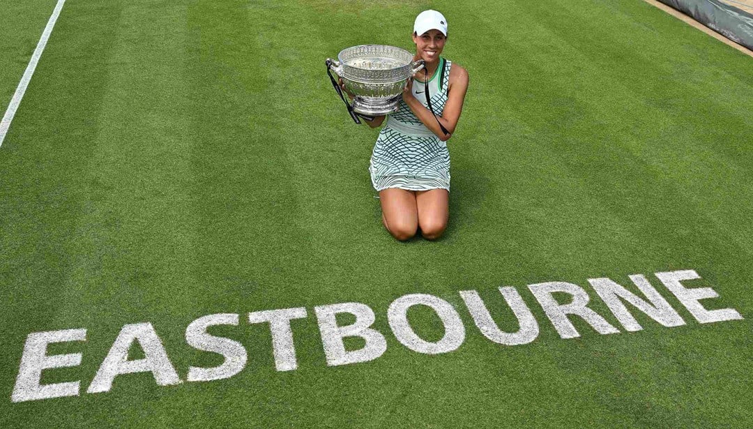 Madison Keys holding the Rothesay International trophy while kneeling down next to the Eastbourne logo on court