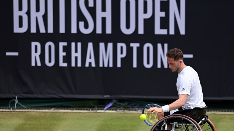 Alfie Hewett bouncing the ball before a serve on grass in front of the Lexus British Open sign