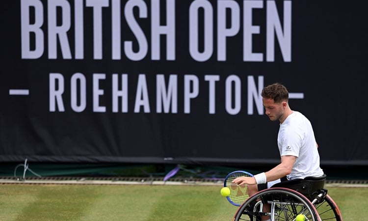 Alfie Hewett bouncing the ball before a serve on grass in front of the Lexus British Open sign