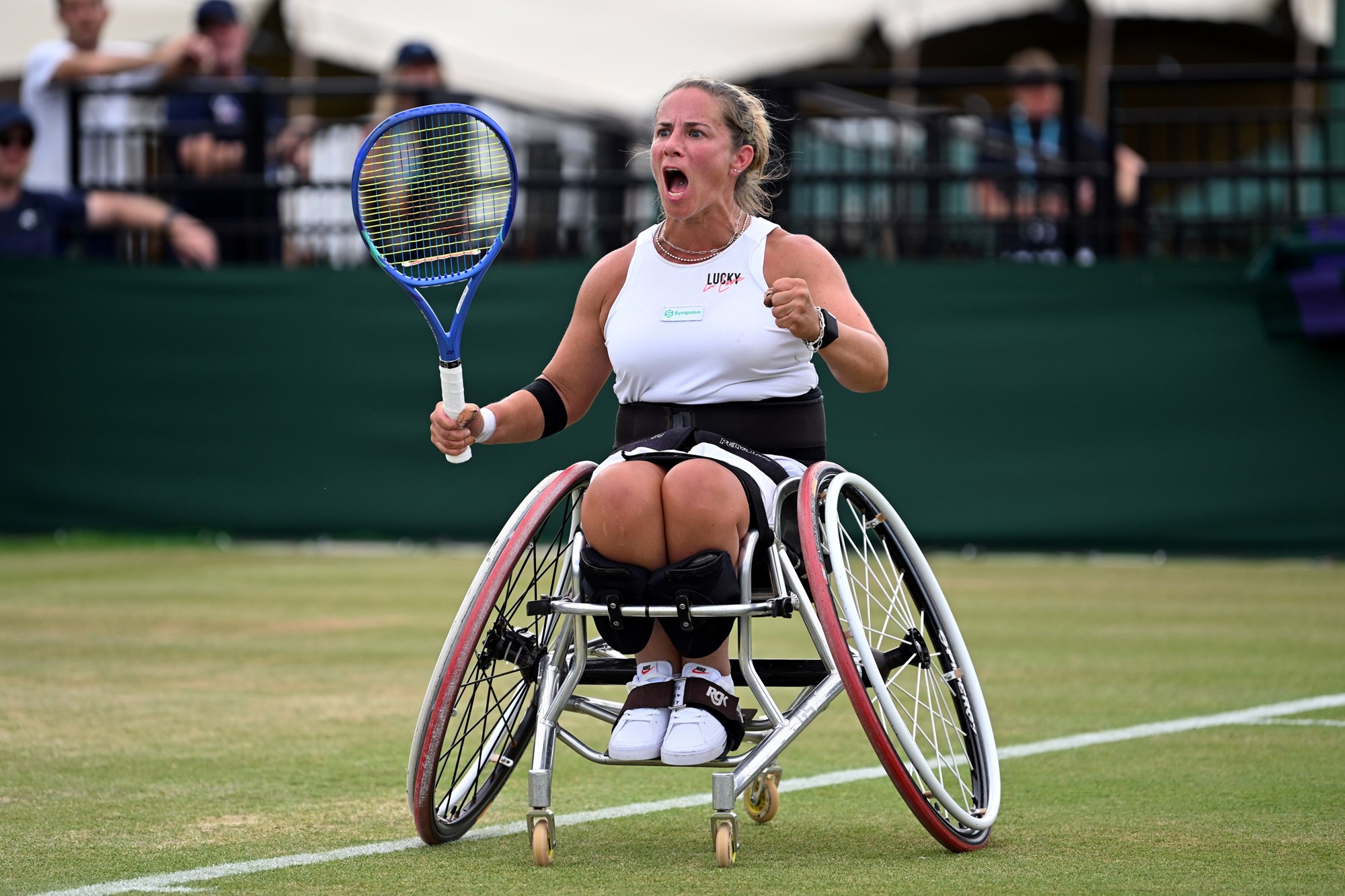 Lucy Shuker roars in celebration on a grass court, with both fists in balls