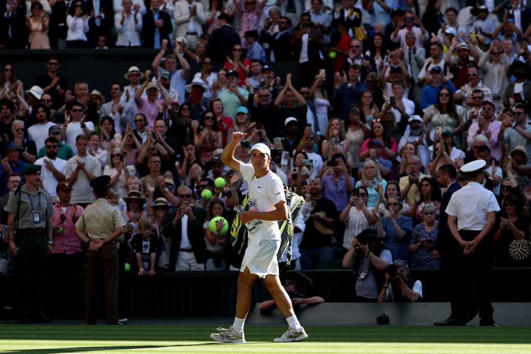 Oliver Tarvet, dressed in white, holding a thumb up to the crowd after his second round match against Carlos Alcaraz at Wimbledon