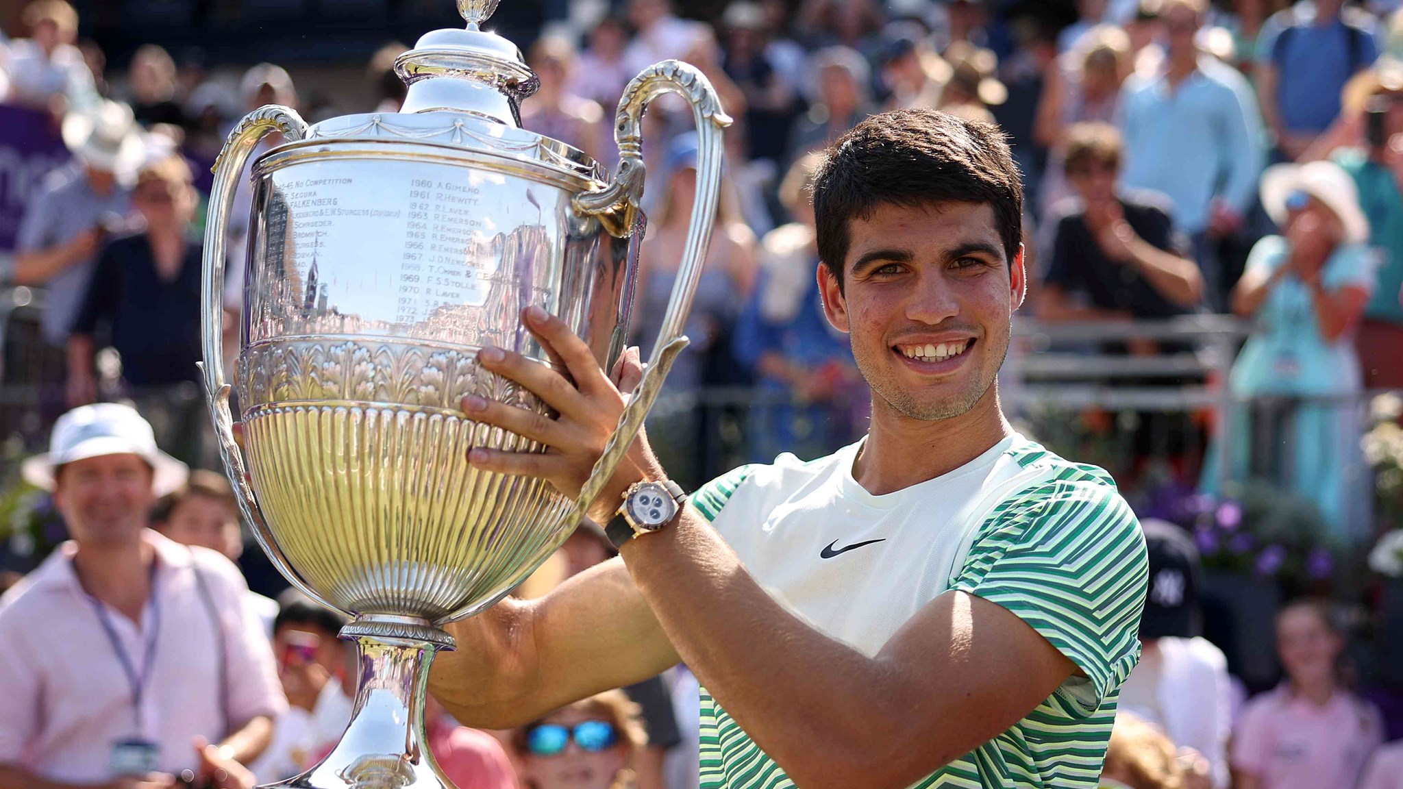 Carlos Alcaraz smiling on court while lifting the cinch Championships trophy