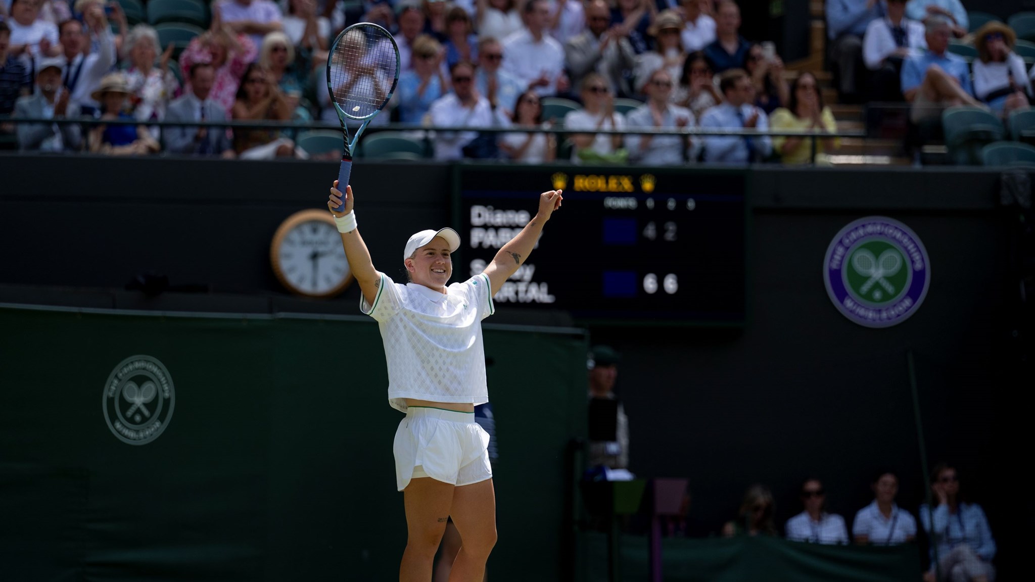Sonay Kartal raises her hands in the air in celebration on the grass court at WImbledon