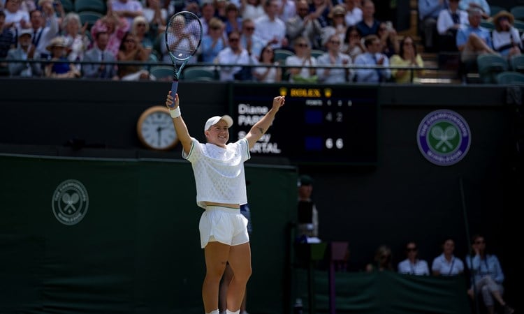 Sonay Kartal raises her hands in the air in celebration on the grass court at WImbledon