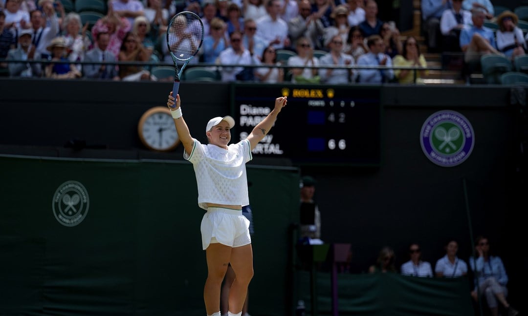 Sonay Kartal raises her hands in the air in celebration on the grass court at WImbledon