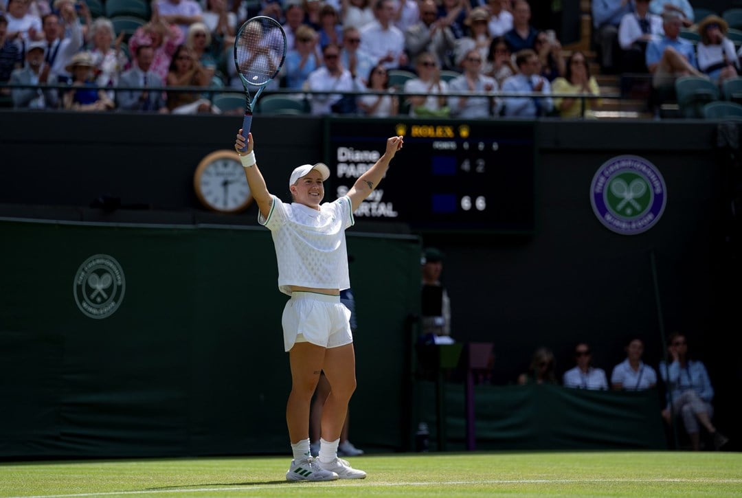 Sonay Kartal raises her hands in the air in celebration on the grass court at WImbledon