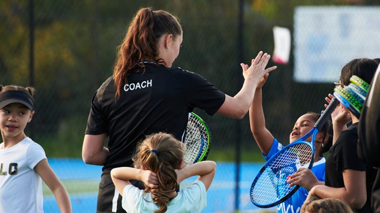 A female coach high fiving a young girl with tennis rackets in their hand