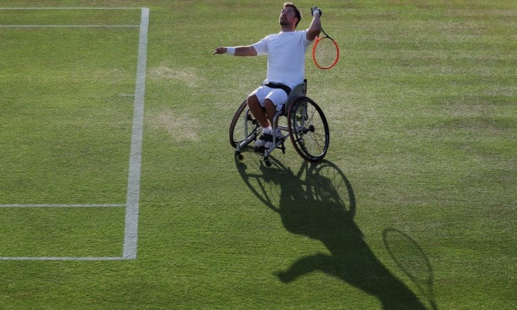 Wheelchair tennis star Sam Schroder about to hit an overheard with his shadow showing on the grass in front of him