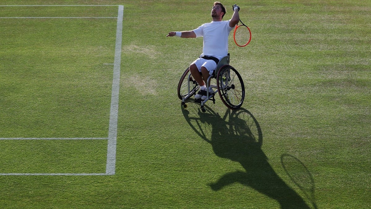 Wheelchair tennis star Sam Schroder about to hit an overheard with his shadow showing on the grass in front of him