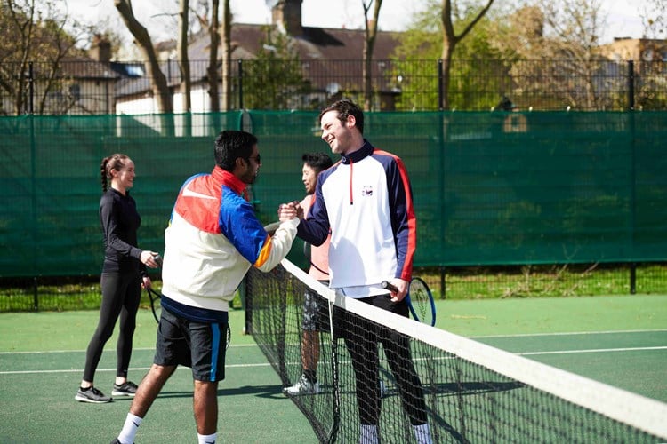 Four people on a tennis court shaking hands at the net