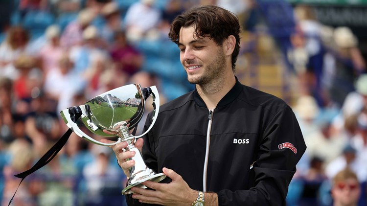 Taylor Fritz smiling and looking down at his trophy on court at the Rothesay International Eastbourne