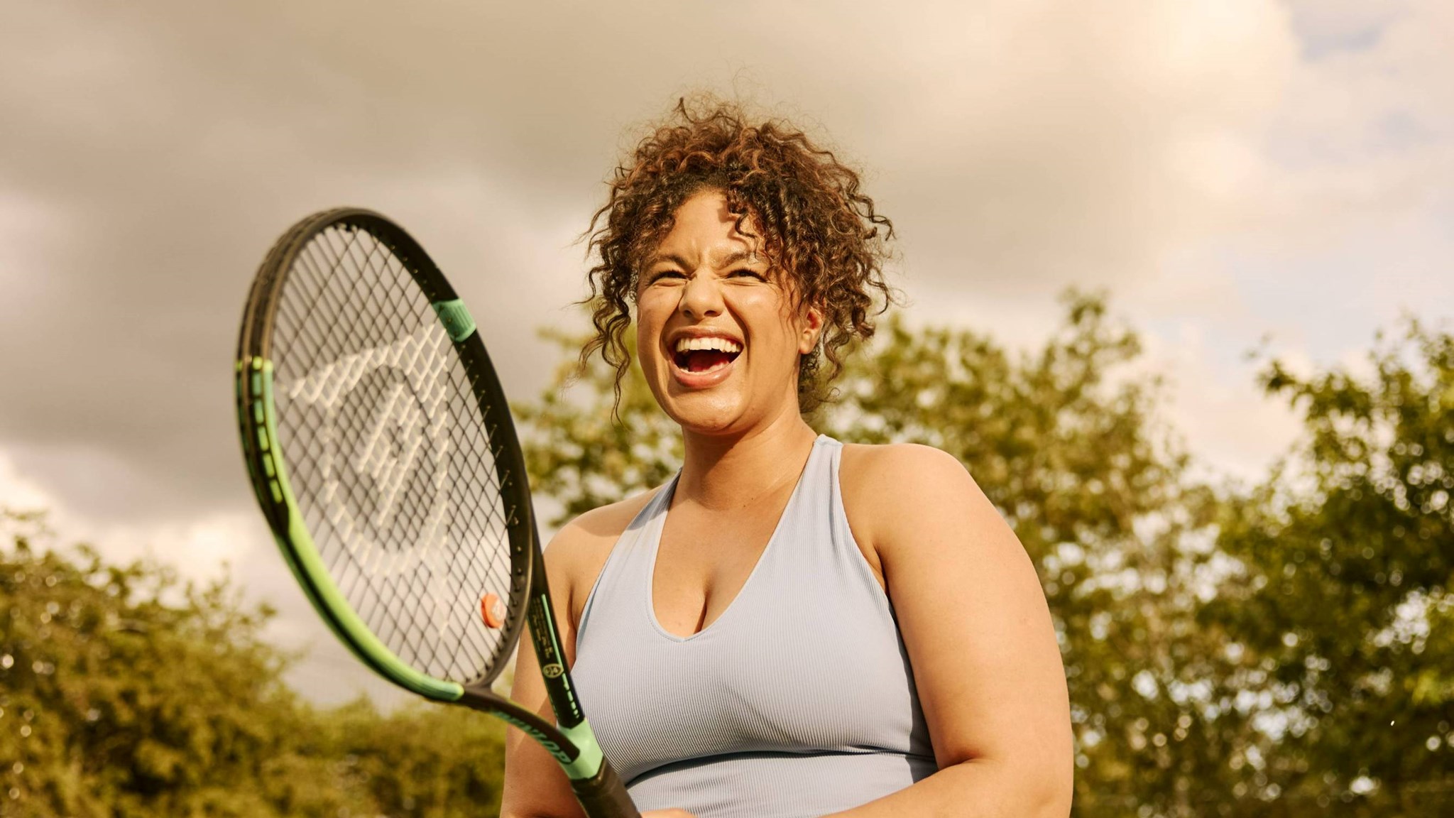 A woman laughing while holding a tennis racket on court