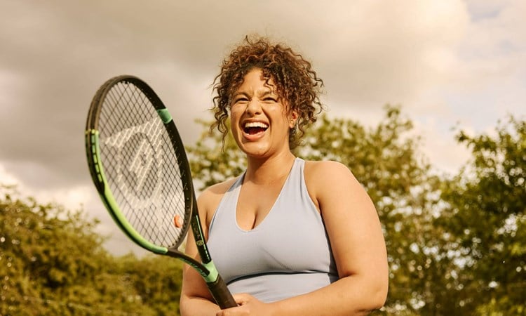 A woman laughing while holding a tennis racket on court