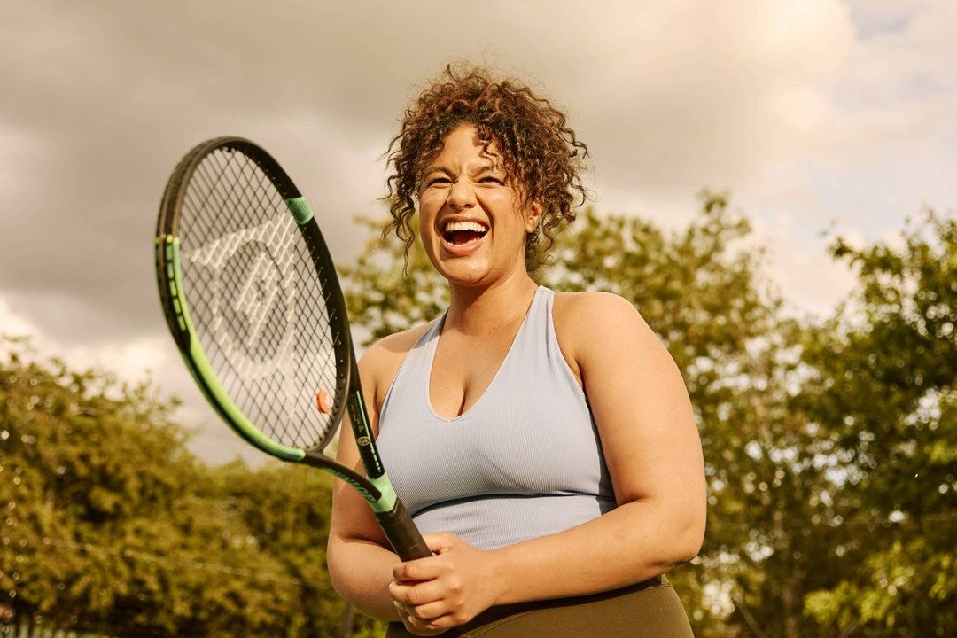 A woman laughing while holding a tennis racket on court