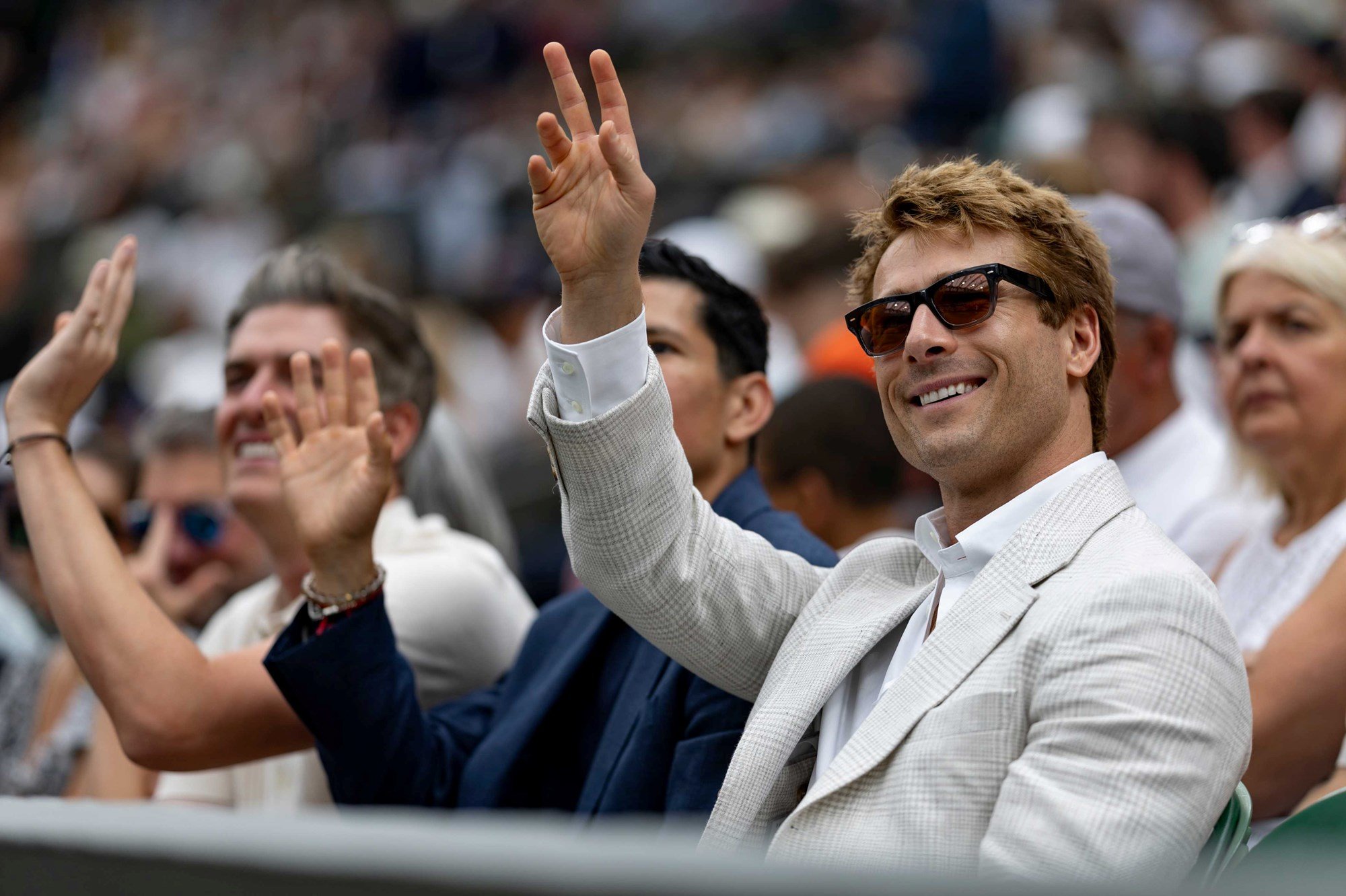 Actor Glen Powell raises his hand to wave to the crowd on Centre Court at Wimbledon