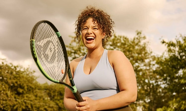 A woman laughing while holding a tennis racket on court